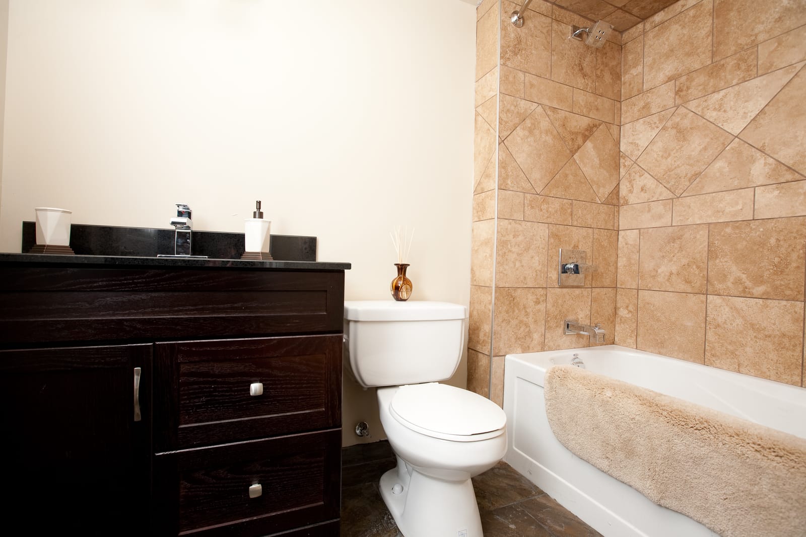 Bathroom with a tiled tub surround and a dark vanity with a granite top